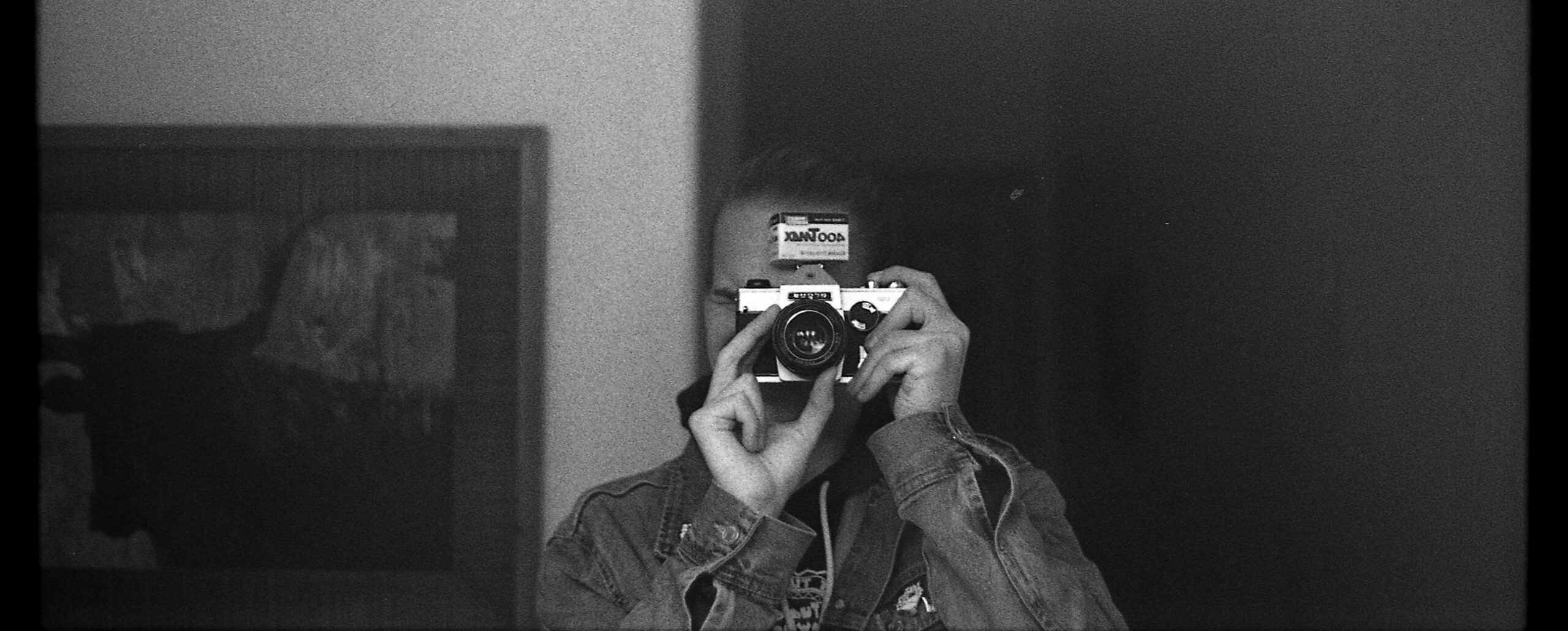 A picture of a person holding a camera and a box of tmax 400 film in a mirror