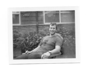 A man sitting in a chair in black and white shot on expired FP-100b film.