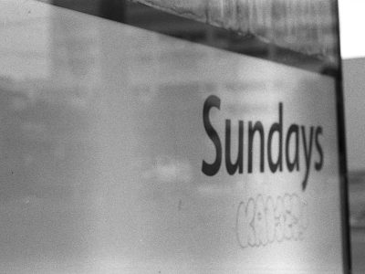 A Black and White image of a sign that says "Sundays" on it with some handwritten graffiti text that is not legible.