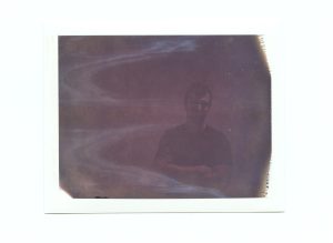 A Dark, improperly exposed polaroid of a man. It is hard to discern his expression or much of his body language.