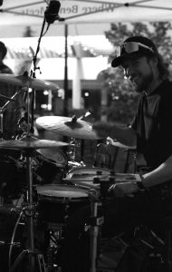 A black and white photo of a drummer at a kit looking at the camera taken on a Canon AE-1.