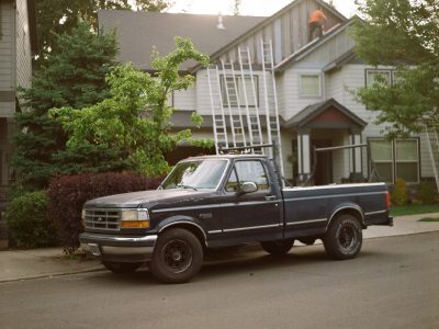 A photo of a truck in front of a house that has several ladders leaning against it.