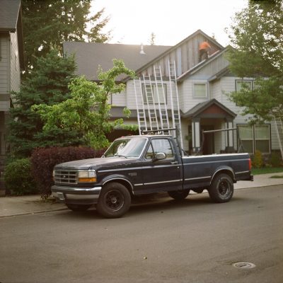 A photo of a truck in front of a house that has several ladders leaning against it.