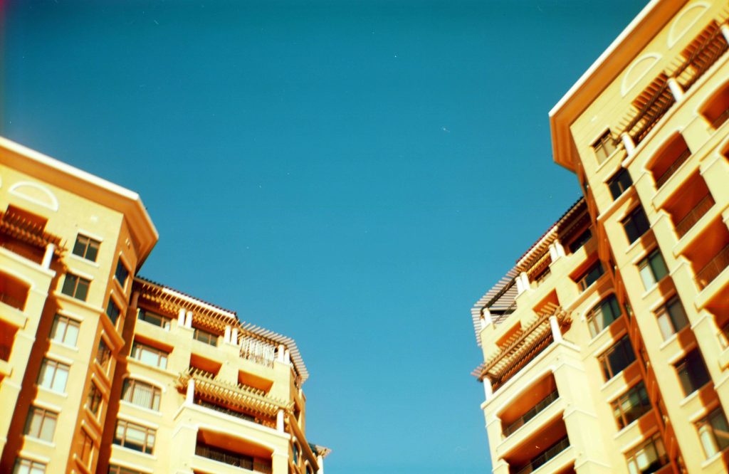 A film photo from a worm's-eye-view of two yellow buildings against a blue Arizona sky.