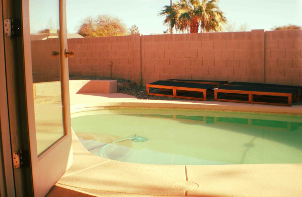 A vintage-feeling film photo on expired film of the doors leading outside with the pool and lounge chairs as the main subject matter. The pool is a light blue, nearly green color in the bright sun.